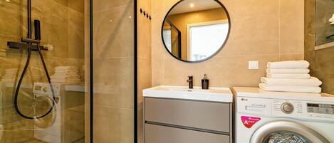 A modern bathroom with a glass-enclosed shower, a sink with a mirror, and a front-loading washing machine.