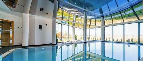 An indoor swimming pool with clear glass walls, a modern architectural design, and a view of the outdoors.