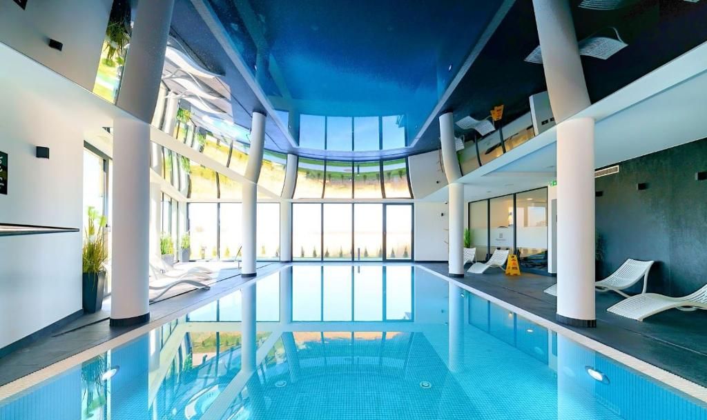 Ein überdachter Schwimmbereich mit großen Glaswänden, weißen Liegestühlen und modernem Design.