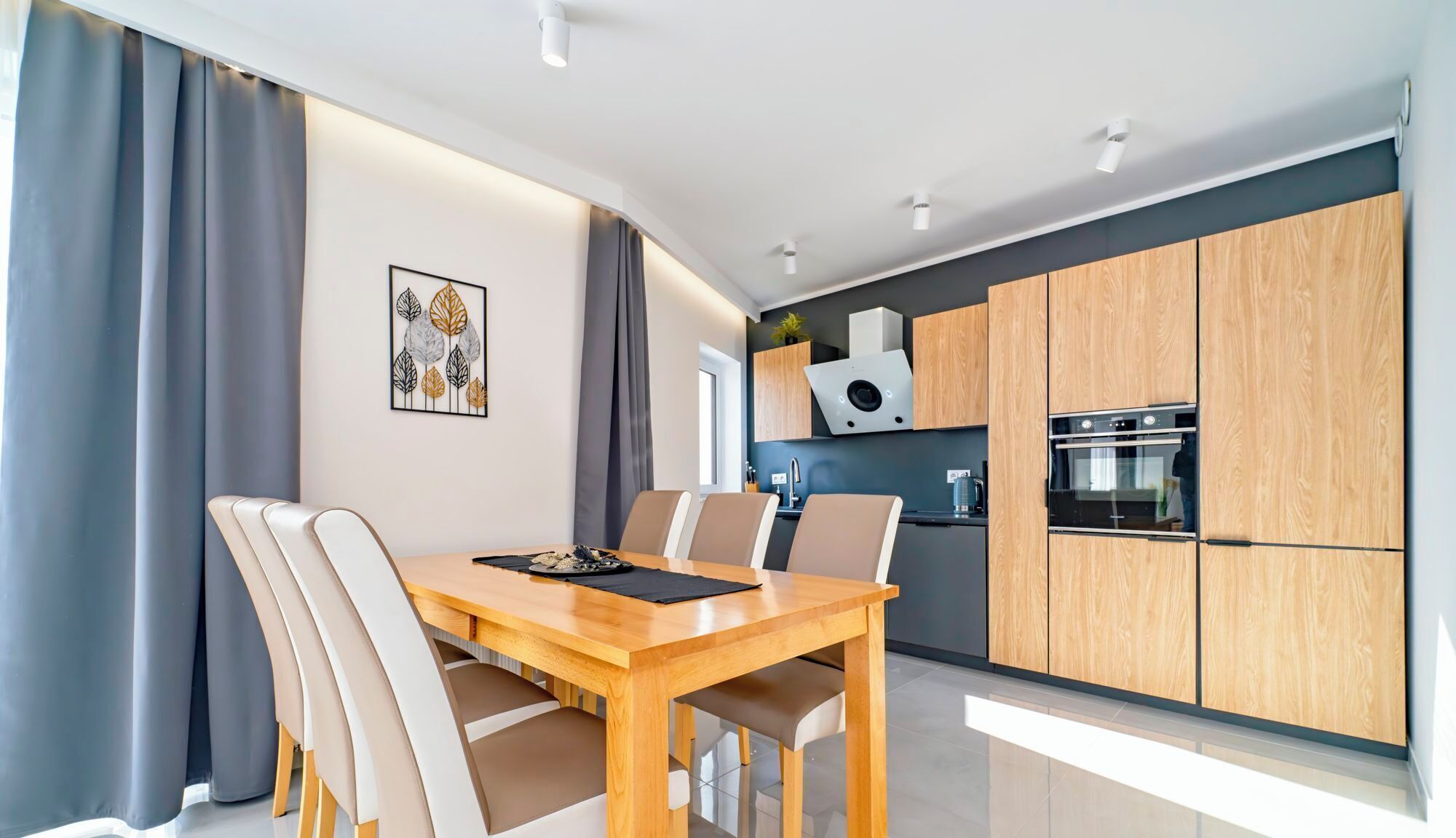 A modern kitchen with wooden cabinets, a built-in oven, and a dining area with a wooden table and chairs.