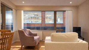 A modern living room with a large window, a sofa, a chair, and a television. - Still Life Clerkenwell Executive (London)