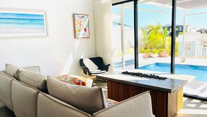 A modern living room with a sofa, a coffee table, and a view of a swimming pool. - Haven 24 - Marina Home (Exmouth)