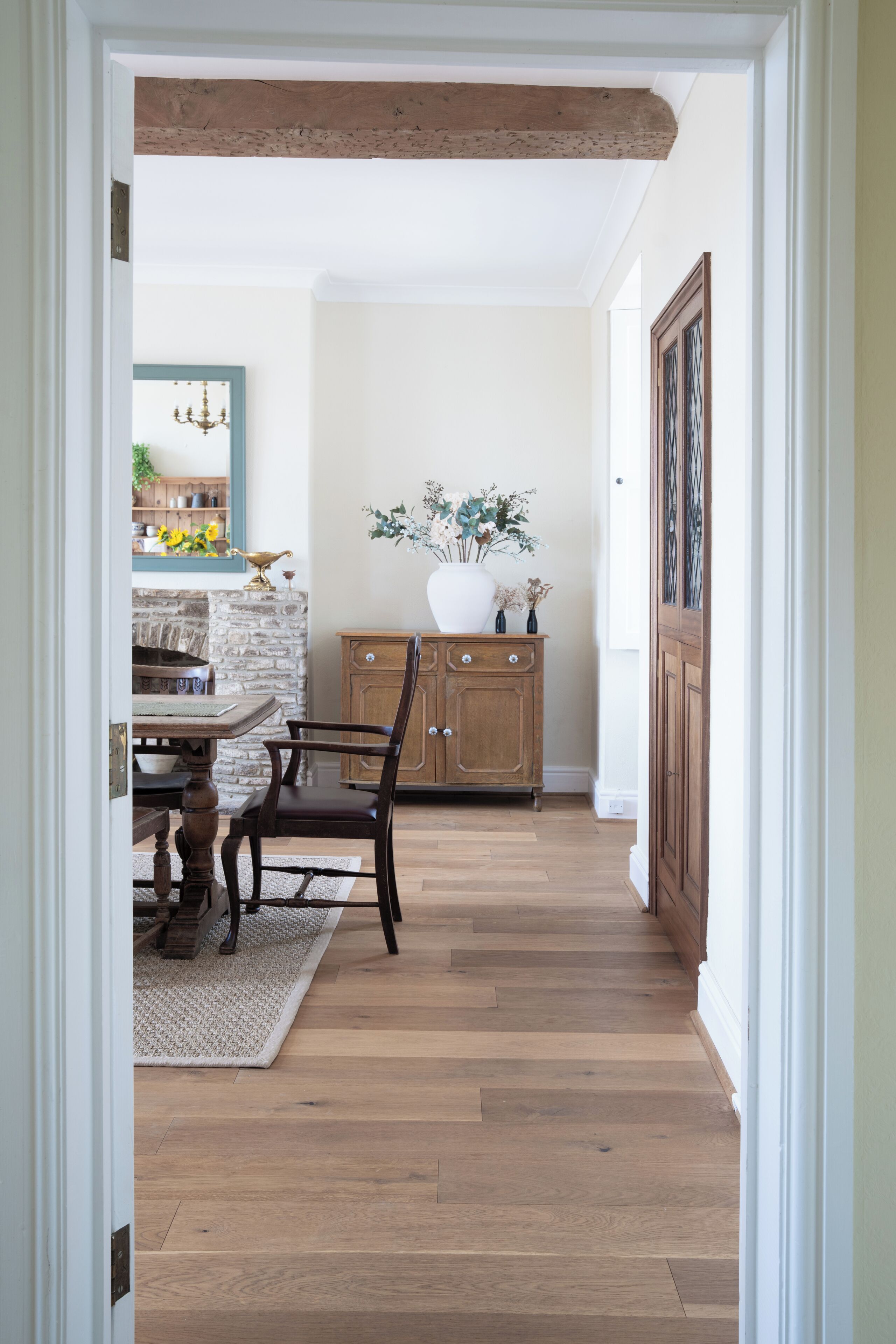 A hallway with wooden flooring, a dining table with chairs, a stone wall, and a cabinet with a vase of flowers.