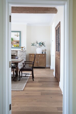 A hallway with wooden flooring, a dining table with chairs, a stone wall, and a cabinet with a vase of flowers. - Manor Farmhouse, Holt, Wiltshire (Near Bath) (Holt)