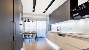 A modern kitchen with a dining area, featuring a large window, pendant lights, and a built-in dishwasher.