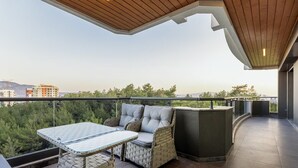An outdoor balcony with wicker furniture, a glass-top table, and a view of the cityscape.