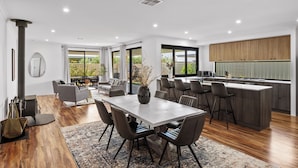 Una cocina moderna con una isla central, un comedor con una mesa grande y sillas, y una sala de estar con sofá y mesa de centro.