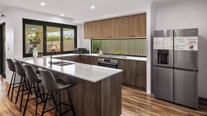 Una cocina moderna con una isla central, taburetes de bar, un refrigerador de acero inoxidable y armarios de madera.