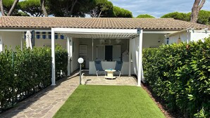 Una villa blanca con tejado de baldosas, un porche cubierto con dos sillas y una mesa, y un césped bien cuidado.