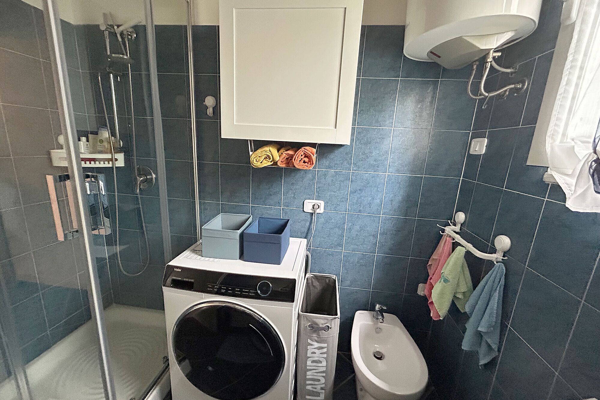 A compact hotel bathroom with a washing machine, a sink, and a shower area.