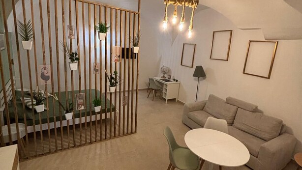 A cozy living room with a sofa, a dining table with chairs, a desk, and a decorative plant wall. - Metro Hause (Napoli)