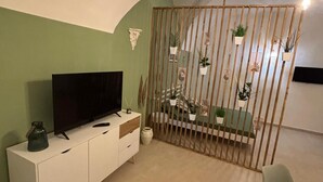 A modern living room with a flat-screen TV on a white cabinet, a green sofa, and a wooden partition with potted plants. - Metro Hause (Napoli)