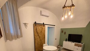 A living room with a sofa, a dining table with chairs, a TV, and a sliding door. - Metro Hause (Napoli)