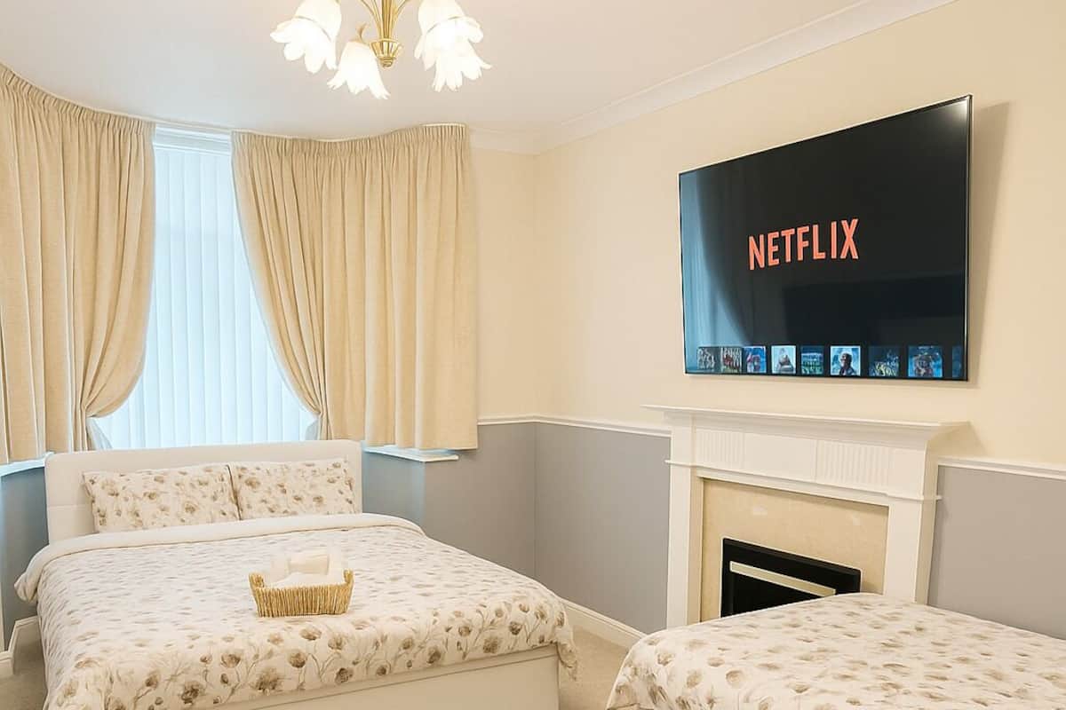 Ett hotellrum med två sängar, en platt-TV som hänger ovanför en öppen spis och ett soffbord i mitten av rummet.