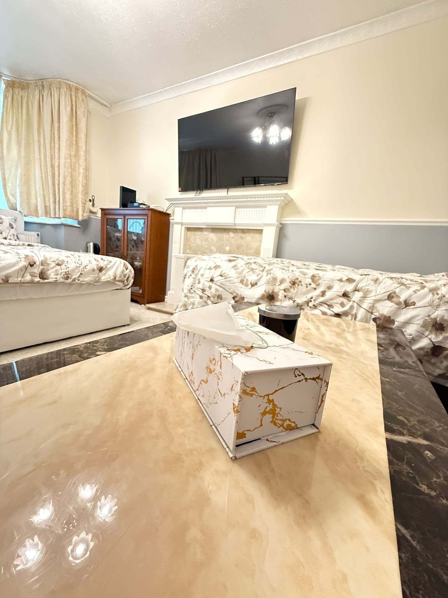 A living room with a sofa, a coffee table, a flat-screen TV mounted above a fireplace, and a window with curtains.