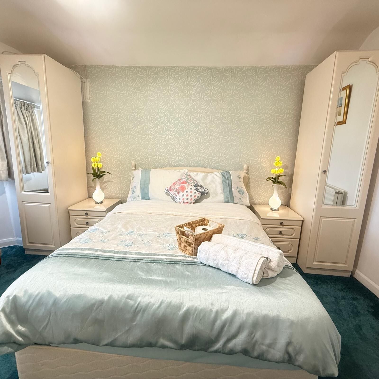 A neatly arranged bedroom with a bed, two bedside tables, a nightstand, a dresser, and a window with curtains.
