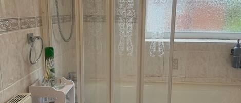 A bathroom with a shower enclosure, a bathtub, and a window with frosted glass.