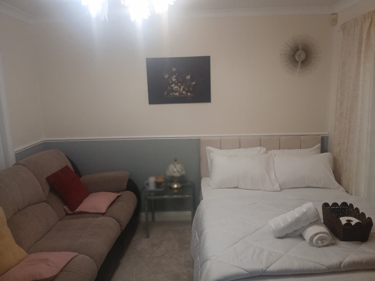 A hotel room with a bed, a sofa, a nightstand, and a wall-mounted artwork.