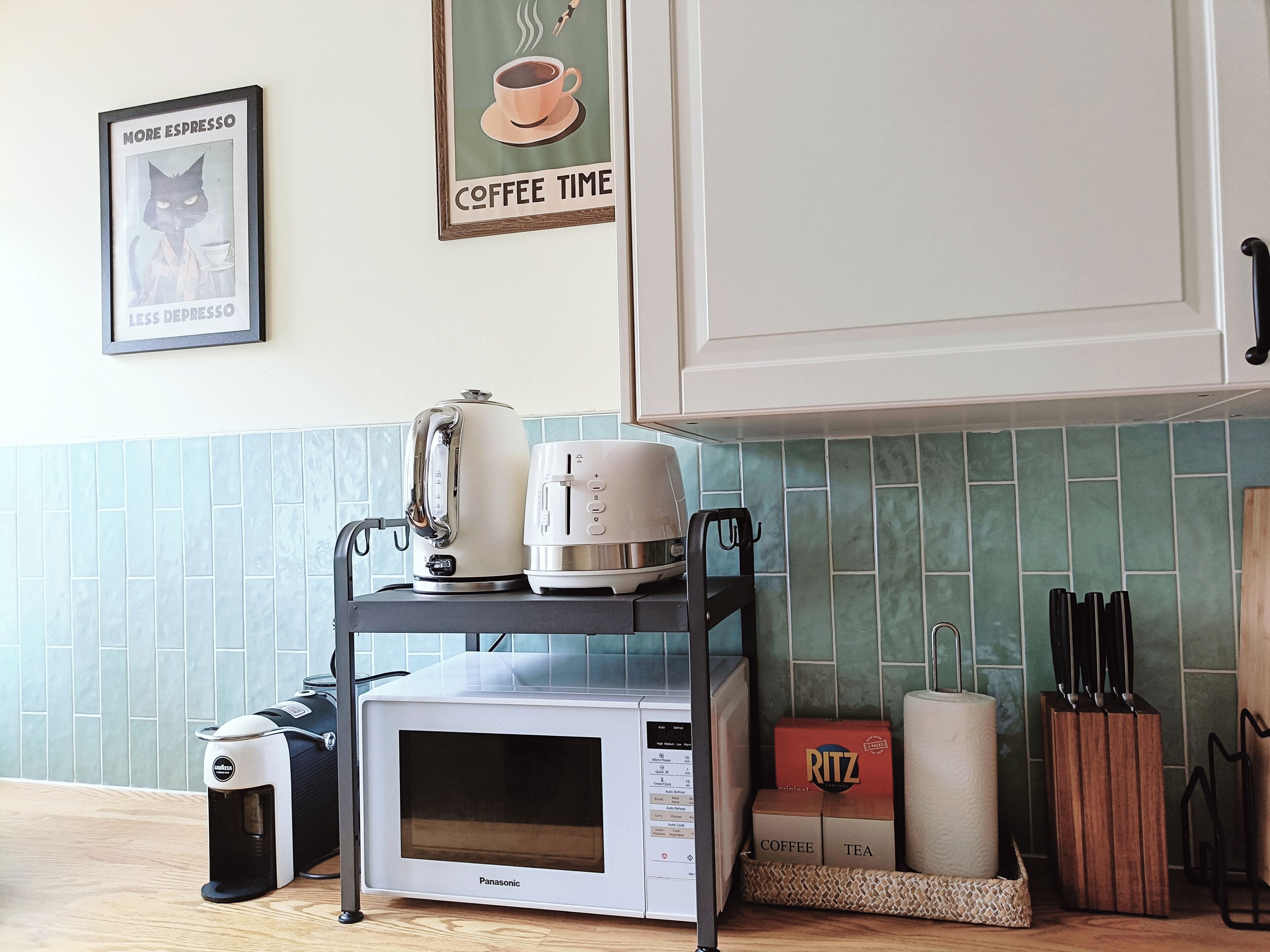 Une cuisine équipée d’un four à micro-ondes, d’un grille-pain et d’une machine à café, le tout posé sur un meuble, ainsi qu’une affiche encadrée sur le thème du café et un placard doté d’une poignée.