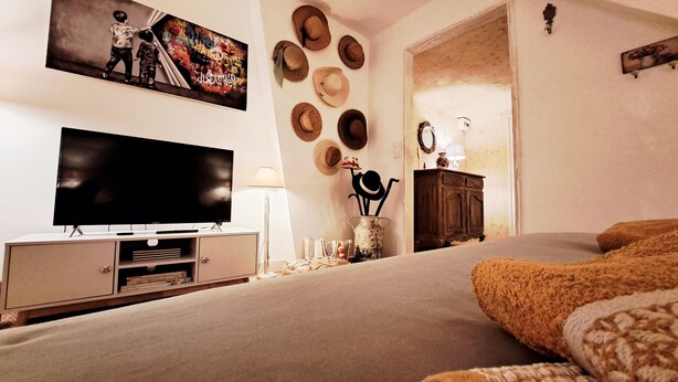A bedroom with a TV, a bed, a dresser, and a wall decorated with hats. - COSY CHAMBER - Air-conditioned SUITE (Sancoins)