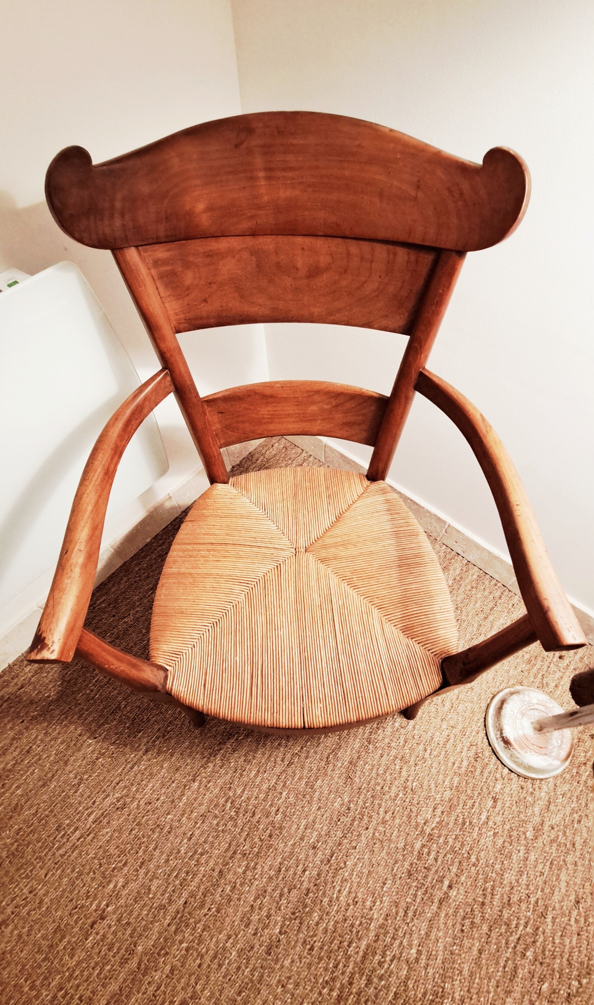 Een houten stoel met een geweven zitting en rugleuning, geplaatst op een vloer met tapijt.