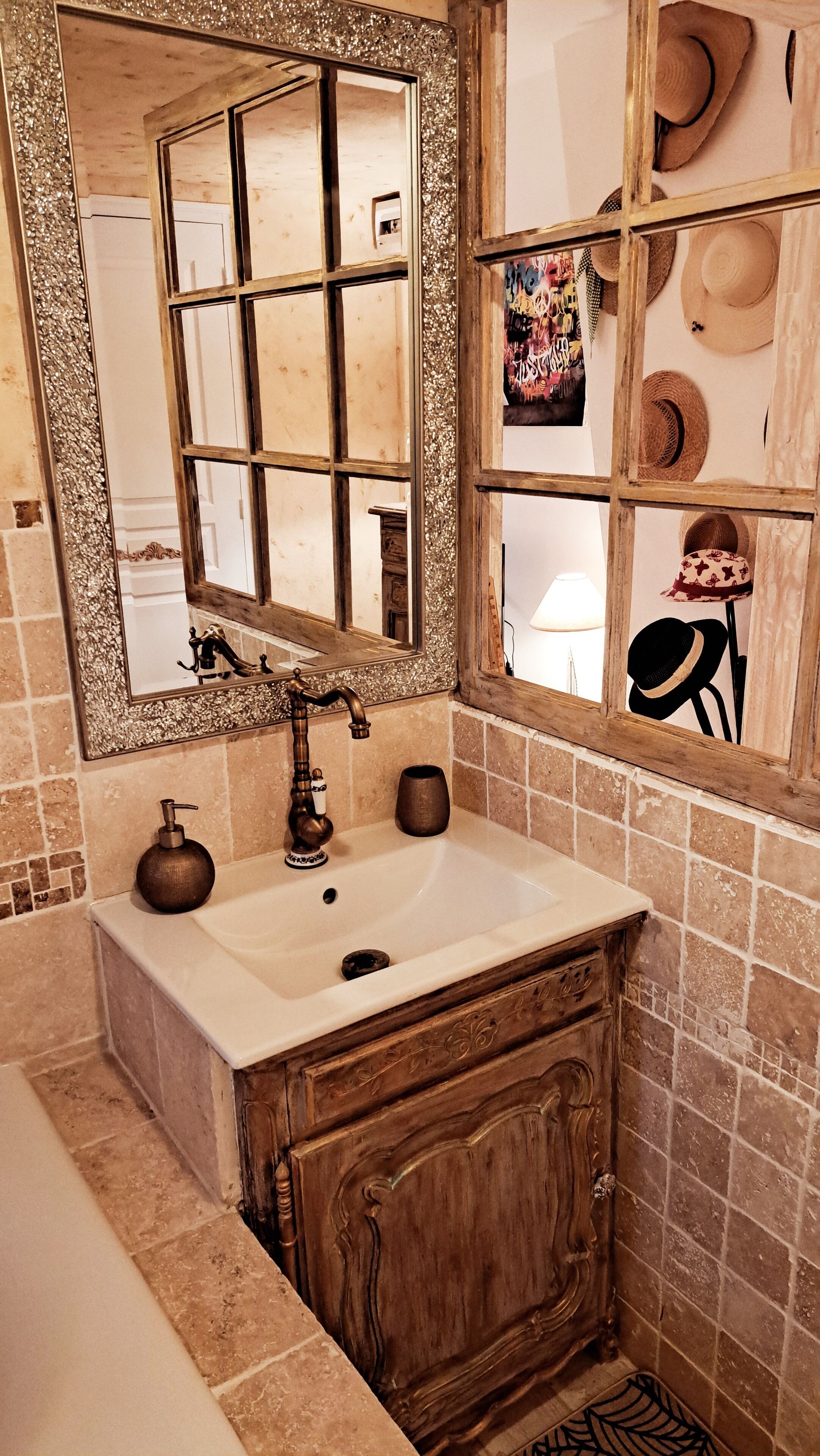 Un baño con lavamanos blanco, mueble de madera y espejo con marco decorativo.