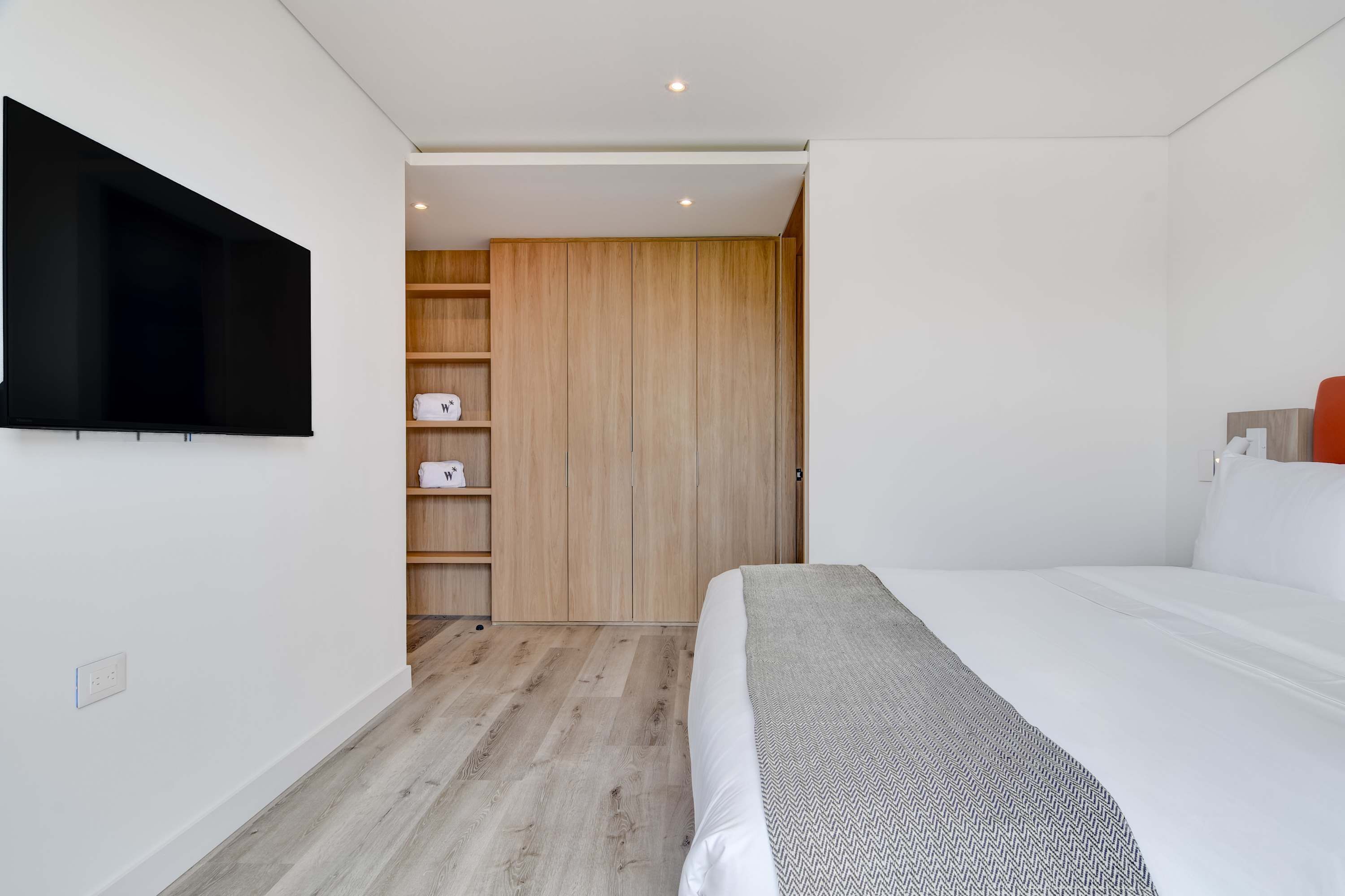 Una camera da letto moderna con un grande letto, una TV a schermo piatto montata a parete, scaffali in legno e un armadio.