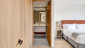 Een moderne slaapkamer met een houten garderobe, een bed met witte beddengoed, en een badkamer met spiegel en wastafel.