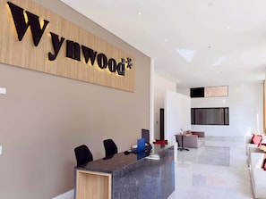 A reception area with a wooden wall displaying the name 'Wynwood'. There is a reception desk with chairs, a laptop, and a small table. The room has a modern design with a large window and a seating area with sofas. - w Startling Loft w Balcony in Santa B Rbara (Bogotá)