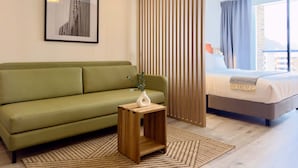A modern hotel room with a green sofa, a wooden side table with a vase, a bed with a view of the city, and a large window with curtains. - w Unfailing Loft w Balcony in Santa B Rbara (Bogotá)