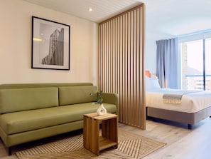 A modern hotel room with a green sofa, a wooden side table with a vase, a bed with a white comforter, a window with curtains, and a framed picture on the wall. - w Unfailing Loft w Balcony in Santa B Rbara (Bogotá)