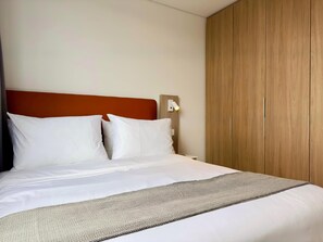 Ein ordentlich bezogenes Bett mit weißer Bettwäsche und einer gemusterten Decke.