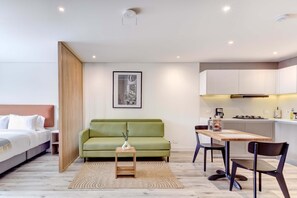 A modern hotel room with a bed, green sofa, dining table, and kitchen area. - w Treasured Loft w Balcony in Santa Barbara (Bogotá)