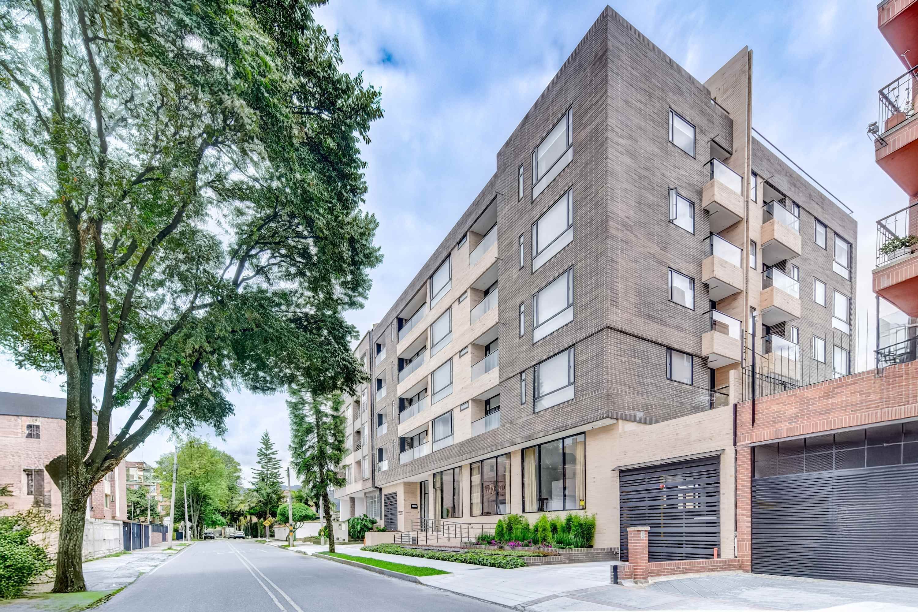 A modern multi-story residential building with balconies, large windows, and a gated entrance.