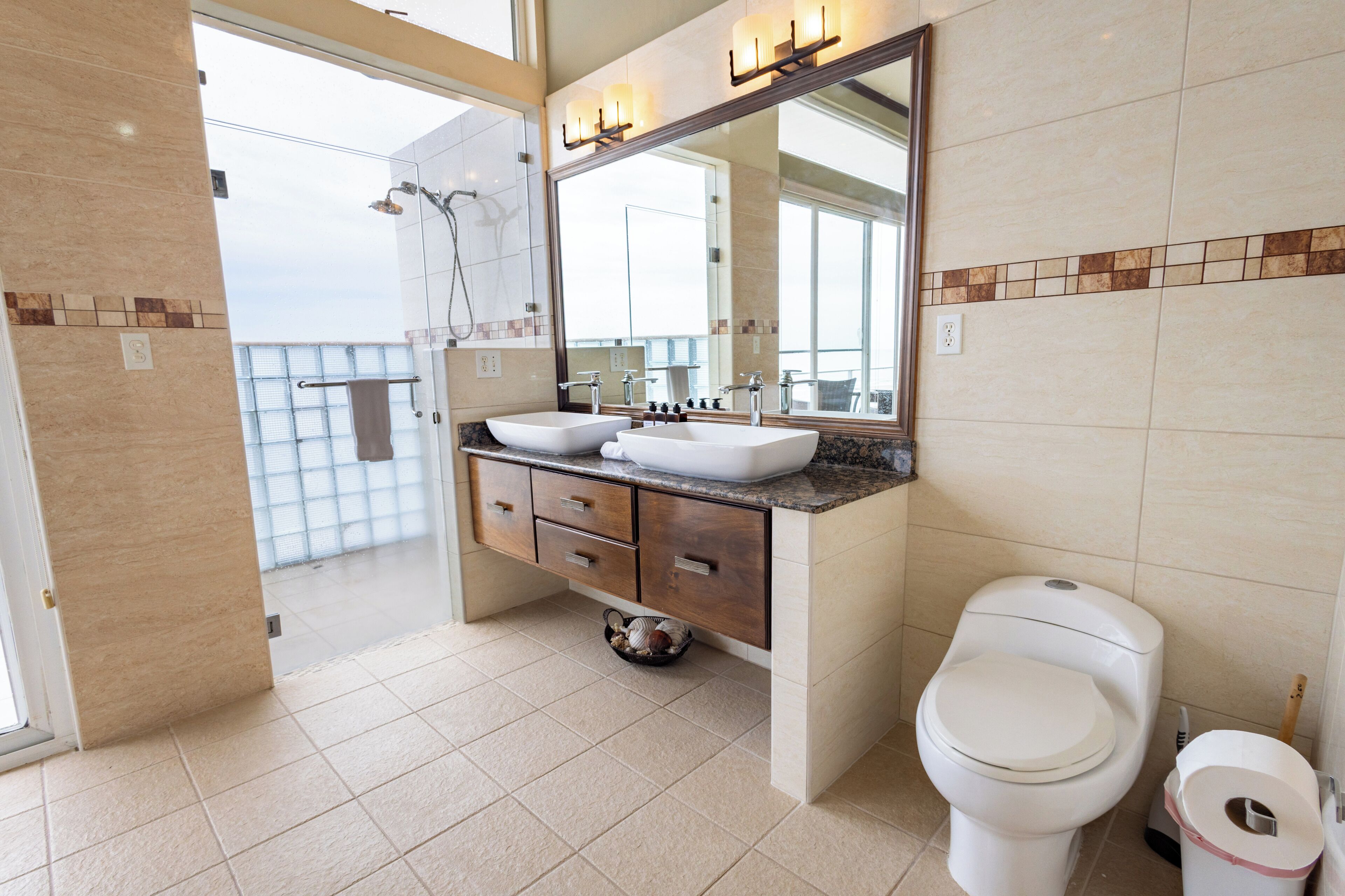 A modern bathroom with a large mirror, two sinks, a toilet, and a shower.