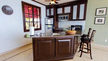 Una cocina con armarios de madera oscura, una isla central, un microondas, un refrigerador y un ventilador de techo.