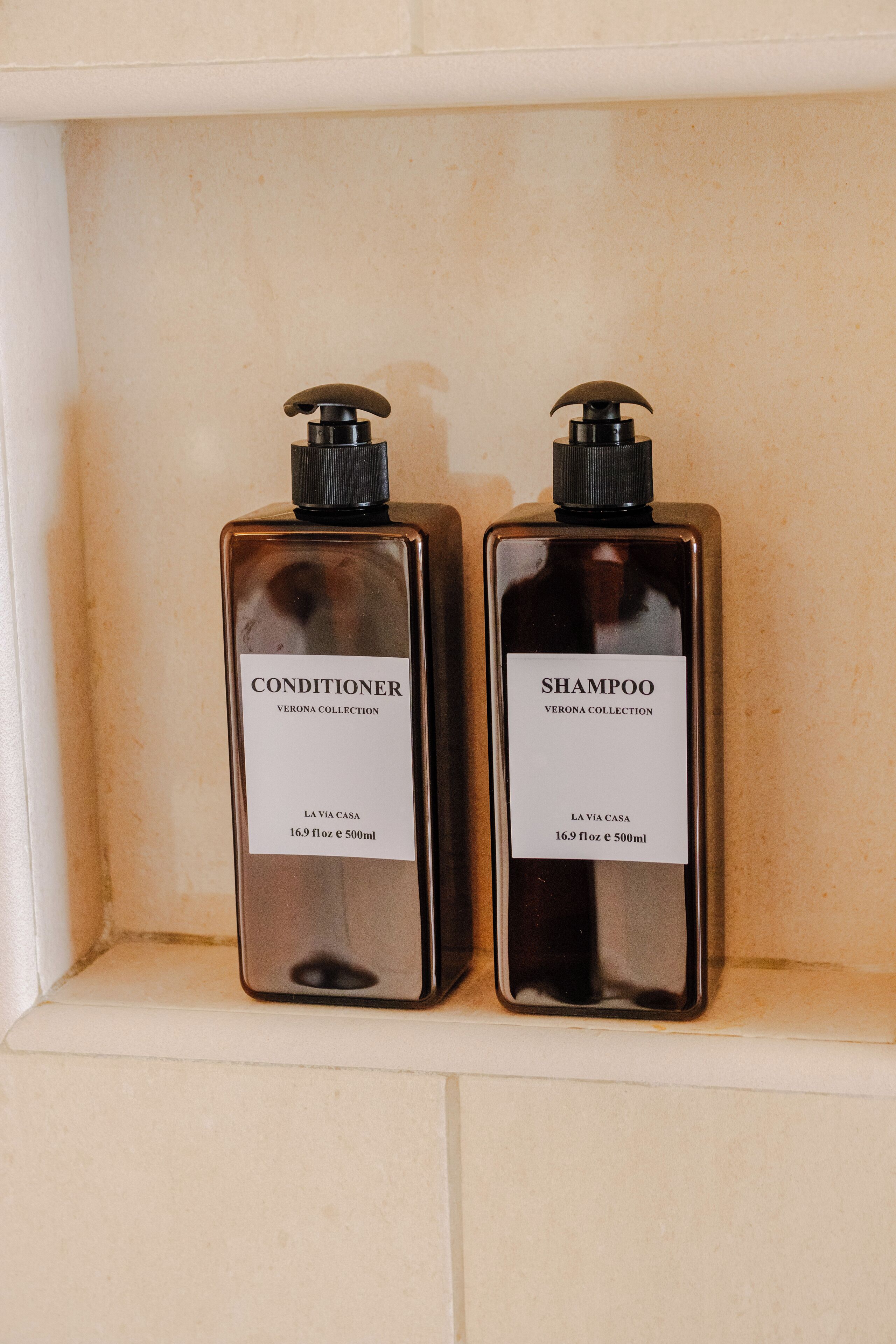 Two bottles of conditioner and shampoo from the Verona Collection, placed in a shelf.