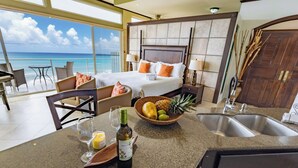 Habitación de hotel con una cama, un área de comedor con mesa y sillas, una cocina con pileta y mostrador, y vista al océano.