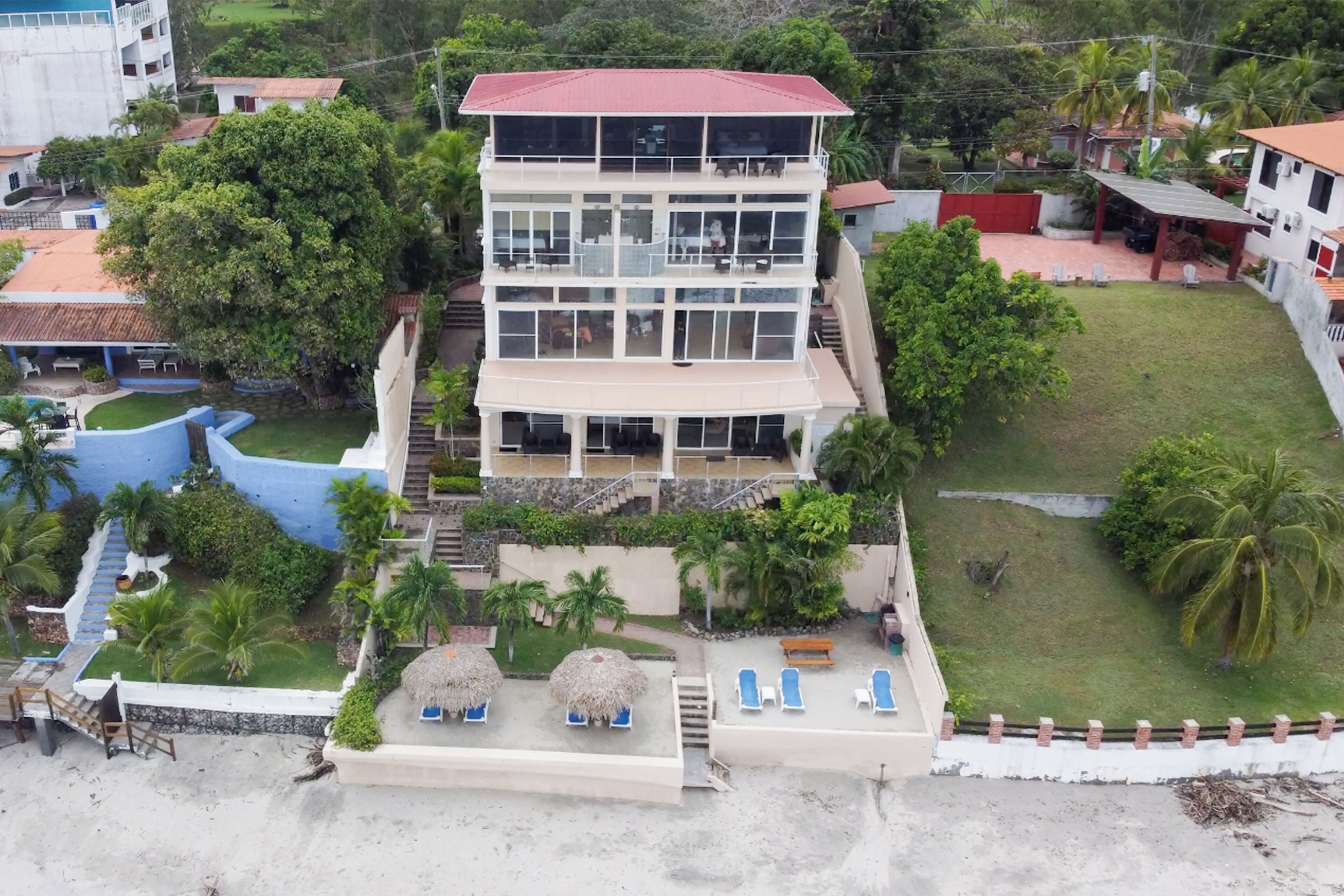A multi-story building with balconies, a swimming pool, and a beach area with lounge chairs.