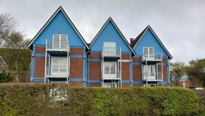 A row of three-story residential buildings with balconies, brick and blue siding, and a hedge in front. - Apartment 'Inselstern' with Balcony and Wi-Fi (Pellworm)