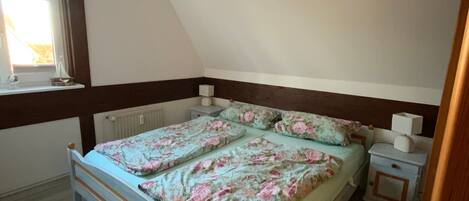 A bedroom with a bed, a nightstand, a window, and a radiator.