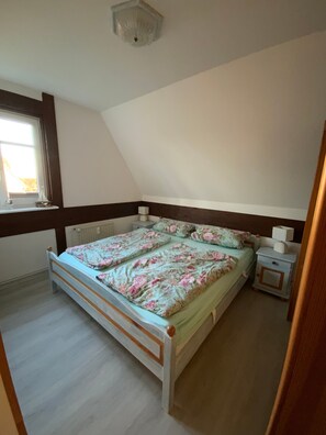 Ein Schlafzimmer mit Bett, Nachttisch, Fenster und Heizkörper.
