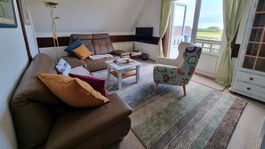 A living room with a sofa, armchair, coffee table, and a view through a glass door. - Apartment 'Inselstern' with Balcony and Wi-Fi (Pellworm)