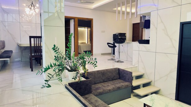 Un lobby moderno con piso de mármol, una zona de estar con un sofá y una mesa de centro, una planta en maceta y un mostrador de recepción con una computadora.