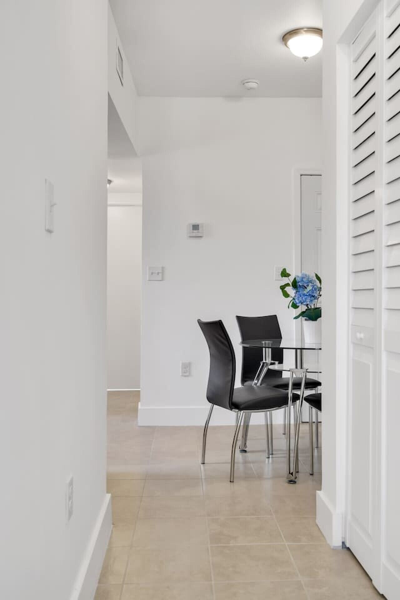 A hallway with a dining area featuring a table and chairs, a small window, and a door with blinds.