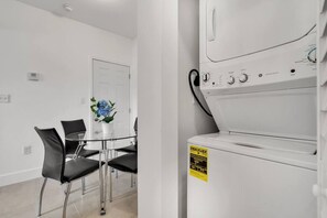 A modern kitchen with a built-in washer and dryer, a glass dining table with chairs, and a potted plant. - Magical 2 BR Apartment - Best Area in Miami ° (Miami)