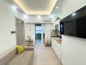 A modern apartment with a kitchenette, a sofa with a yellow pillow, a small table with a plant, and a sliding glass door leading to a balcony. - Athens Luxury Penthouse (Athens)