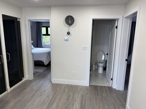A modern bedroom with a bed, a bathroom with a toilet, and a hallway leading to another room.