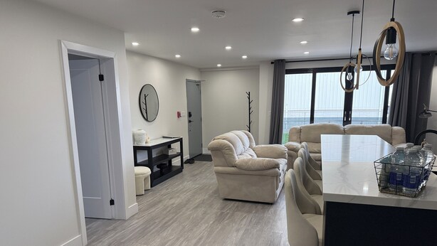 A modern living room with a sofa set, a dining area with bar stools, and a kitchen counter with water bottles.