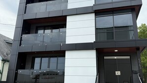 A modern multi-story building with a flat roof, large windows, and a staircase leading to the entrance.